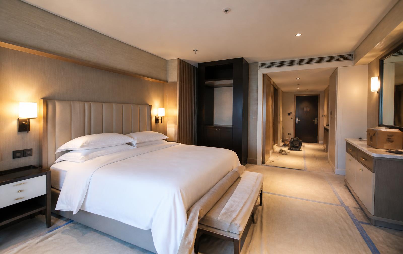 Upscale hotel guest room mid-renovation with finished furnishings and construction underway in the corridor